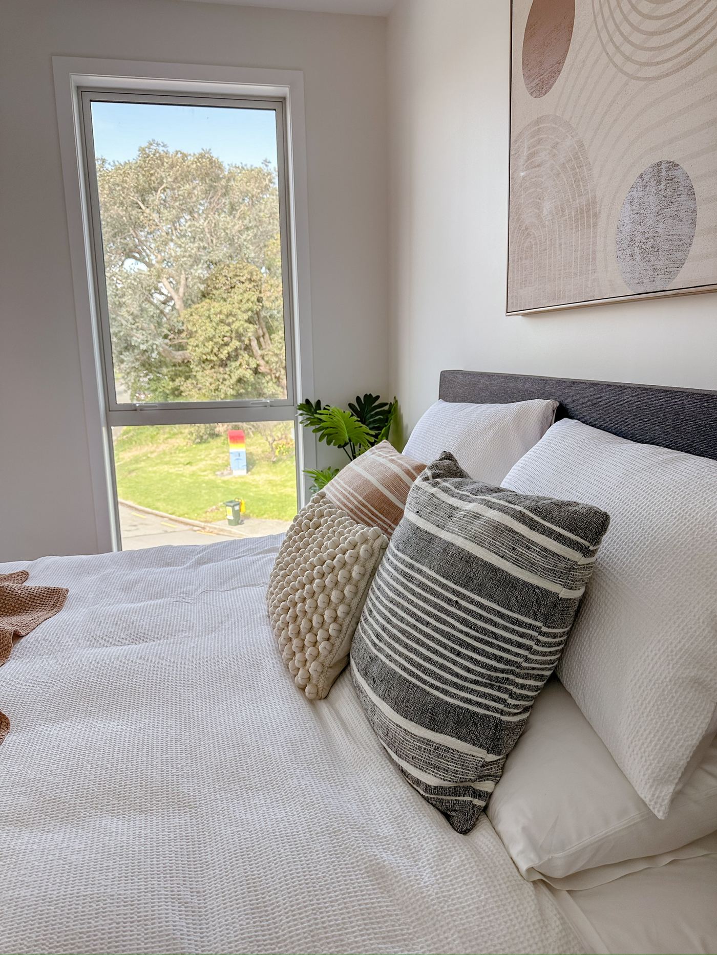 Bedroom with layered cushions and a window view of trees